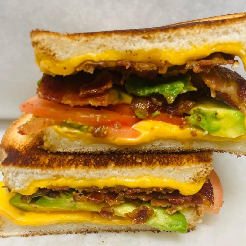 A toasted sandwich from Waverly Deli, cut in half, revealing bacon, avocado, tomato, and melted cheese.