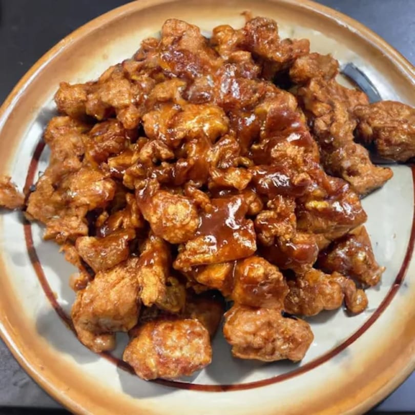 A plate of golden-brown, bite-sized chicken pieces coated in a glossy, dark sauce.