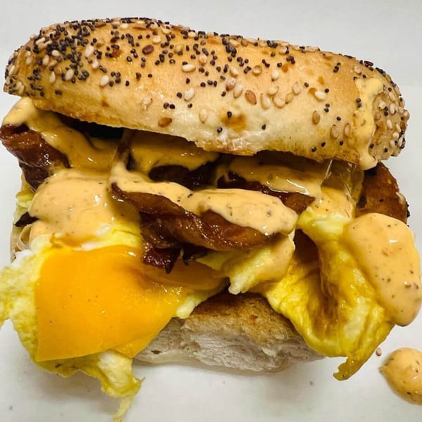 A Waverly Deli breakfast sandwich with eggs, bacon, cheese, and sauce on a seeded bagel.