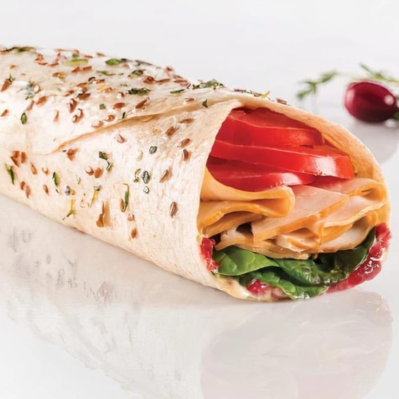 Waverly Deli turkey wrap with tomatoes, spinach, and cranberry sauce on a white surface.