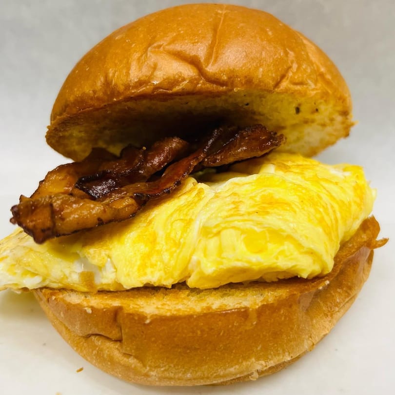 A Waverly Deli breakfast sandwich with scrambled eggs and bacon on a toasted bun.